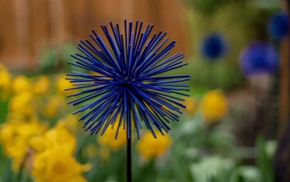 a blue metal allium sculpture in front of daffodils 