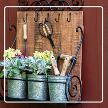 Wall Shelf with Planters with flowers planted in them and small garden tools, all hanging on a red wooden wall