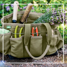 Gardener's Puddle Proof Tote filled with garden tools on mulched path in front of garden