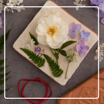 Terra Cotta Flower Press on table with flower petals, ribbon, and ferns around