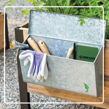 Galvanized Tool Storage Box with gardening tools inside hanging on the side of an elevated garden bed