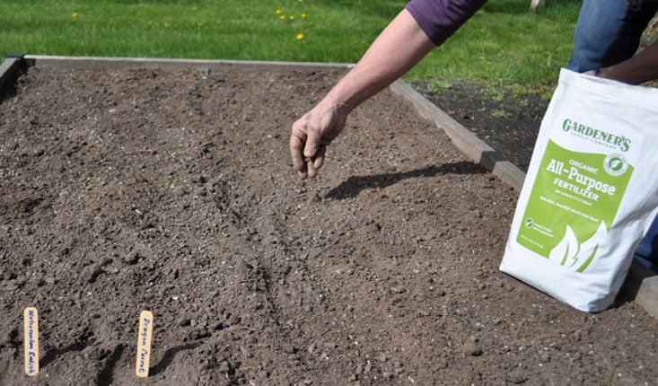 Gardener's All Purpose Organic Fertilizer being sprinkled on soil in raised bed
